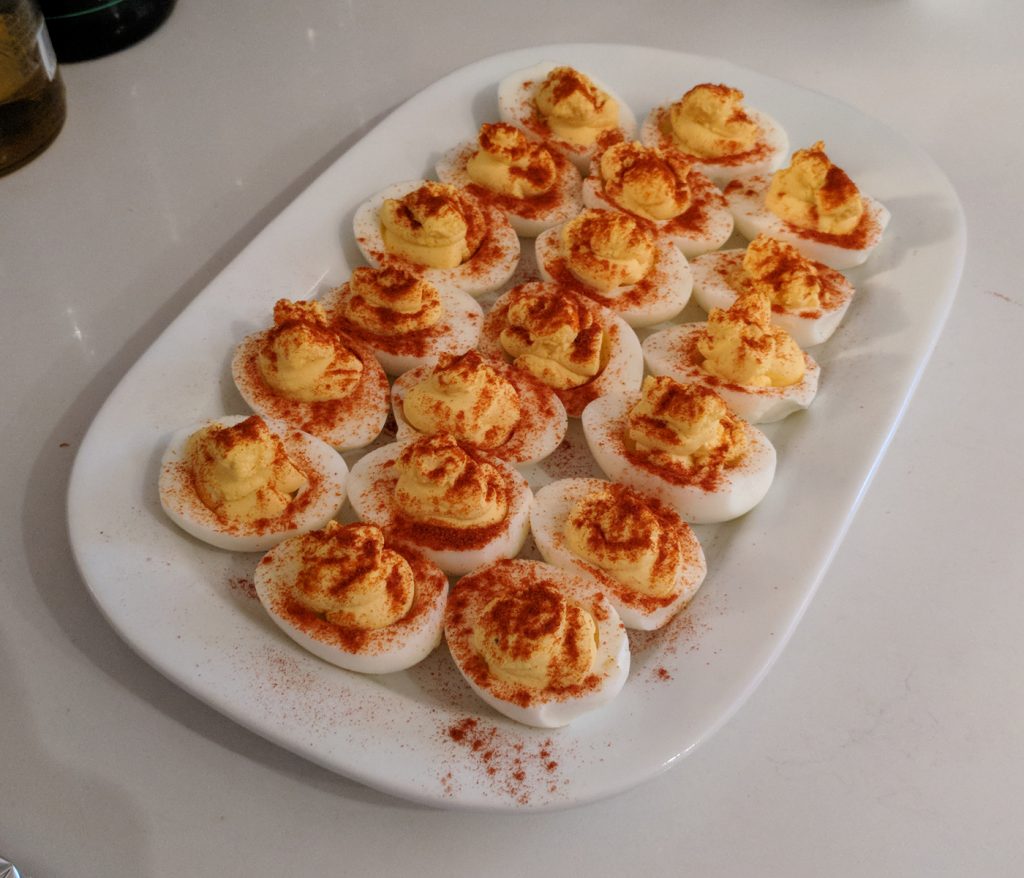 three rows of deviled eggs with a LOT of paprika on a rectangular white plate on a white countertop