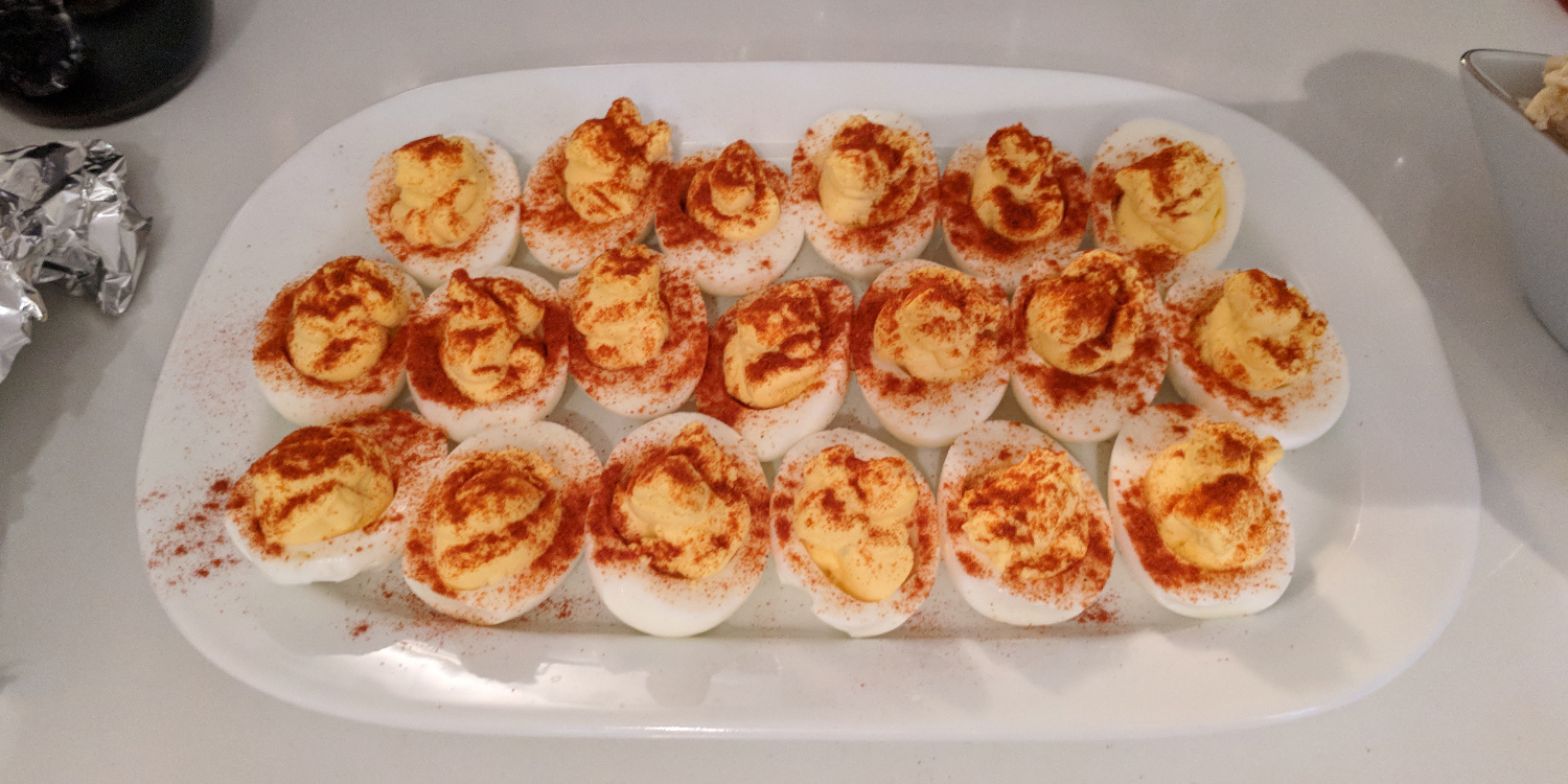 twenty deviled eggs with a LOT of paprika arranged in three rows on a rectangular white plate