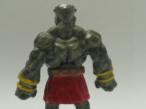 A stone golem mini from the back, painted grey, red and gold.