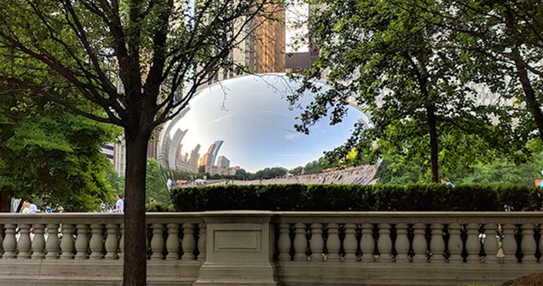 Chicago's Cloud Gate, or Bean, as seen from outside its pavilion with trees surrounding it.